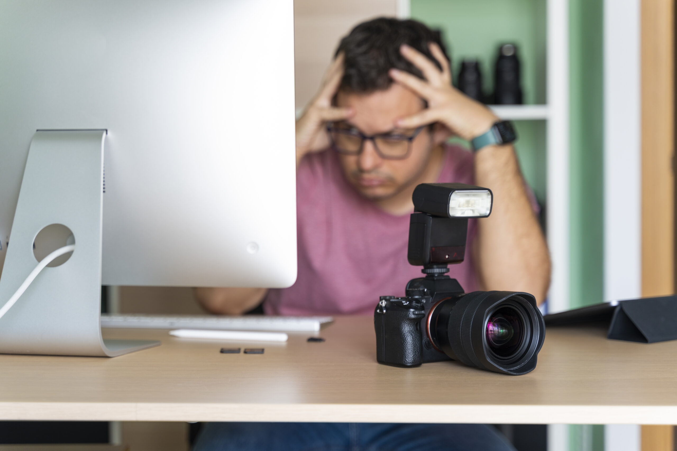 Ein Fotograf sitzt vor seinem iMac und guckt verzweifelt