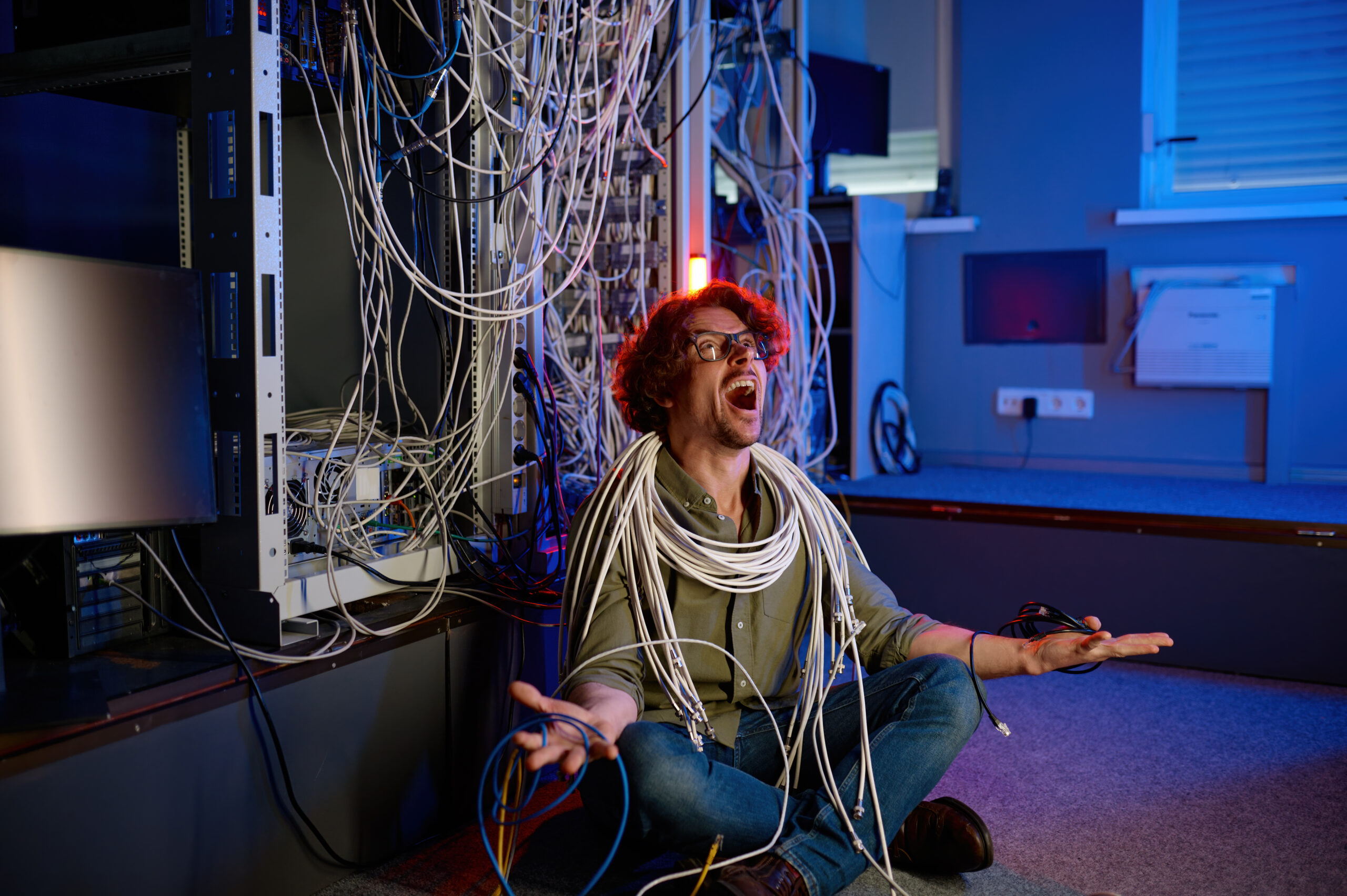 Gestresster Netzwerker sitzt vor seinem Server in Kabel gewickelt